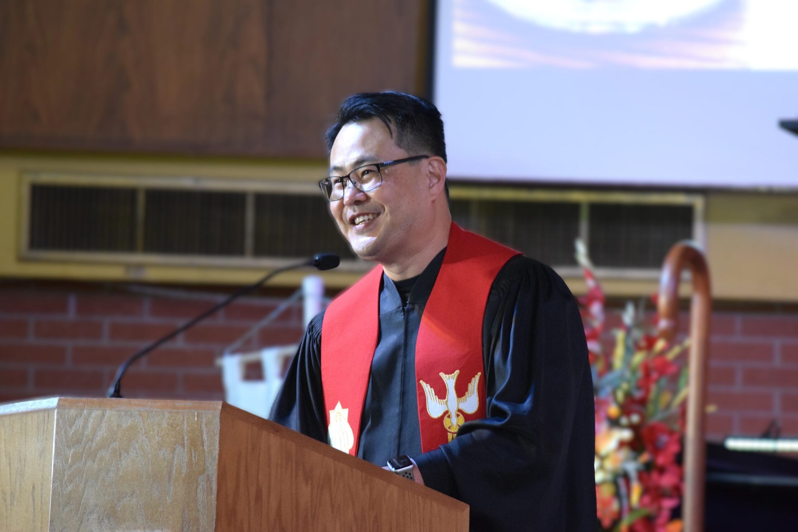 Pastor Young preaching at a wooden pulpit, wearing a red ordination stole